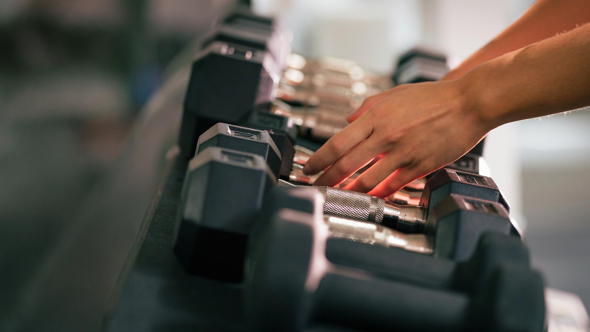 Kädet nostamassa käsipainoja kuntosalilla.