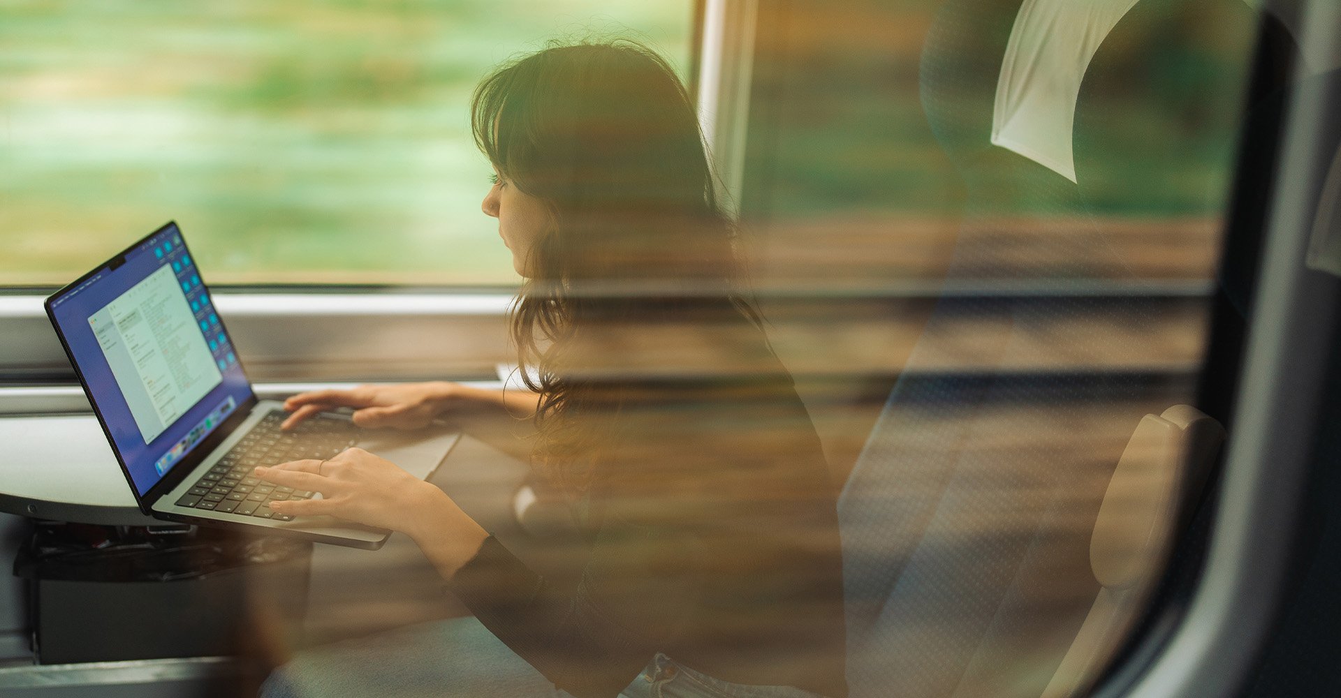 Henkilö työmatkalla junalla tekemässä töitä läppärillä.