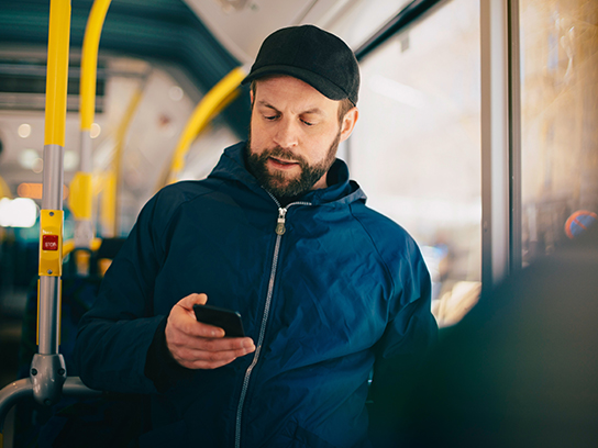Mies selaamassa puhelintaan julkisen liikenteen kulkuneuvossa työmatkalla.