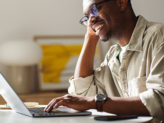 Hymyilevä henkilö nojaa käteensä ja selaa tietokonetta.